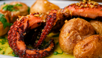 Grilled octopus tentacle with roasted potatoes on a white plate.