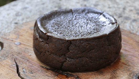 Round chocolate cake on a wooden board with a cracked surface.