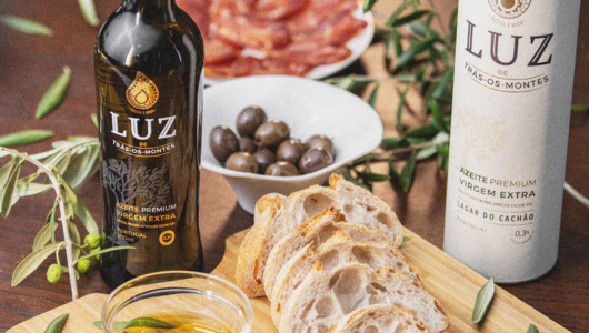 Olive oil bottles, sliced bread, olives, and salami on a wooden table.
