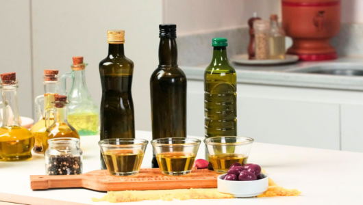 Bottles and glasses of olive oil on kitchen counter with olives and spices.