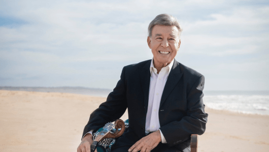 Smiling man in a suit sitting on the beach with ocean in background.