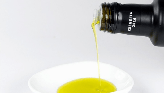 Olive oil pouring from bottle into white bowl on white background.