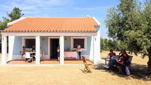 Small house with red roof; people sitting outside on a sunny day.