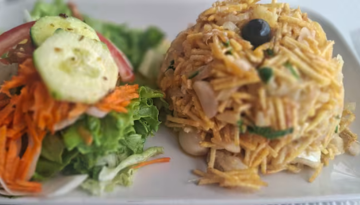 Salad with cucumber slices and shredded carrots beside a mound of noodles topped with an olive.