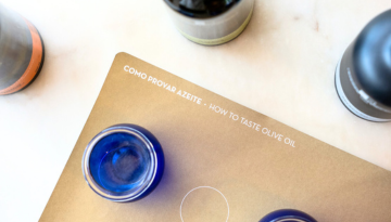 Blue cups on a 'How to Taste Olive Oil' mat with bottles nearby.