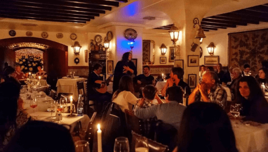 Dimly lit restaurant with people seated, musicians performing in background.