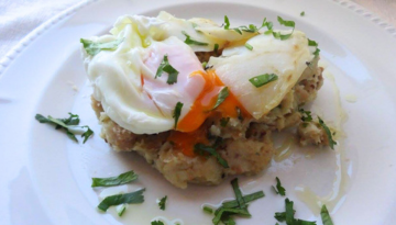 Poached egg with runny yolk on mashed potatoes, garnished with herbs on a white plate.