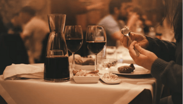 Dining table with wine, food, and person holding fork in cozy restaurant setting.