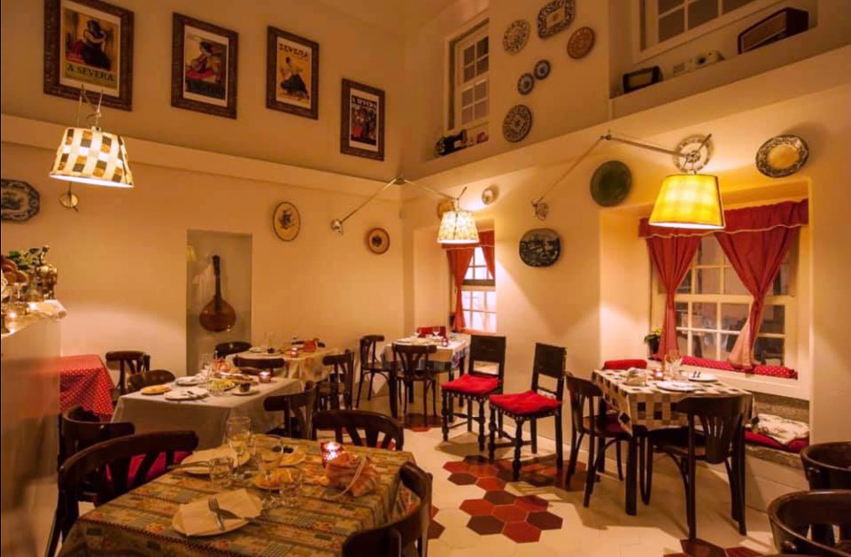Cozy restaurant interior with tables, red cushioned chairs, wall decor, and warm lighting.