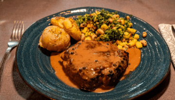 Steak with sauce, roasted potatoes, and mixed vegetables on a blue plate.