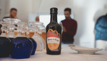 Bottle on a table with glasses and people in the background.