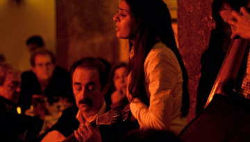 Musician playing guitar and woman singing in a dimly lit venue.