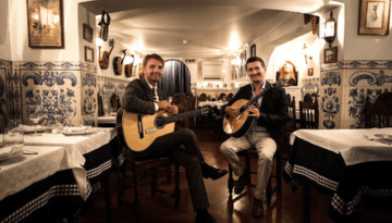 Two men with guitars sitting in a decorated restaurant with blue tiles.