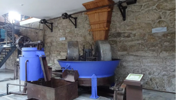 Vintage machinery with stone wheels and blue container against a stone wall.