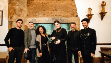 Group of six people smiling in front of a rustic fireplace.