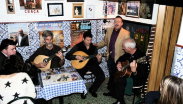 Group playing string instruments inside a decorated room with blue patterned walls and framed art.