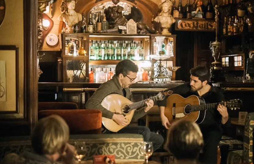 Two musicians playing guitars in a cozy, vintage bar setting.