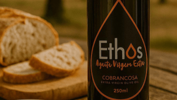 Bottle of Ethos extra virgin olive oil beside sliced bread on a wooden table.