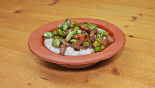 Clay bowl with a dish of beans, diced vegetables, and grain on a wooden table.