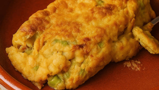 Close-up of a golden-brown omelette with visible vegetables on a plate.