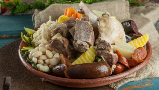 Plate with assorted meats, sausages, beans, and vegetables on a rustic background.
