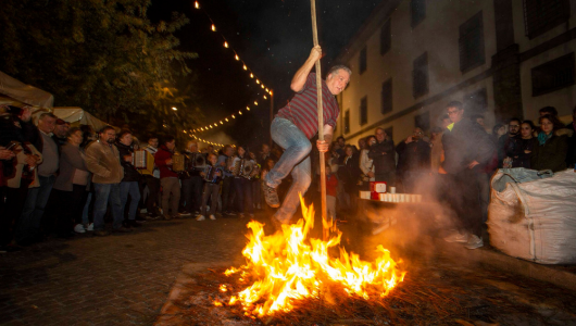 Person balancing on a stick over a fire in front of a crowd at night.