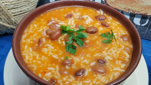 A bowl of tomato-based soup with rice, beans, and parsley garnish on top.