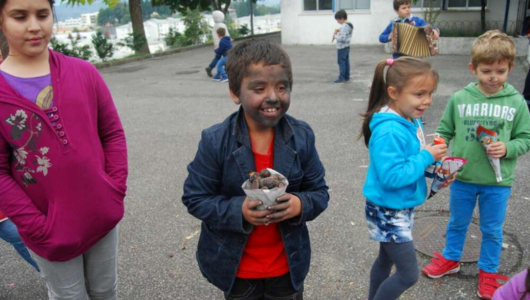 Children playing outdoors, one boy smiling with face painted black, holding a bag.