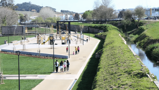 People walking in a park with a playground and a nearby stream.