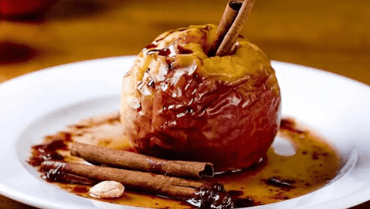 Baked apple with cinnamon sticks and sauce on a white plate.