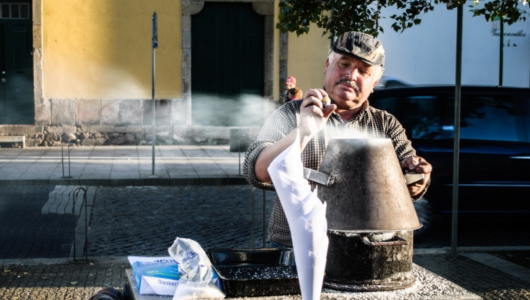 Man making candy floss outdoors with machine and sugar cone in a sunny street setting.