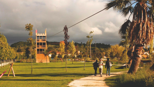 Three people walking on a path through a park with a tower and trees.