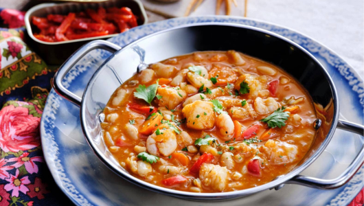 Seafood stew with shrimp and vegetables in a blue bowl on a floral tablecloth.