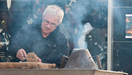 Man cooking at outdoor market stall surrounded by smoke.