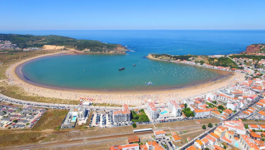 Aerial view of a coastal city with a crescent-shaped beach and clear blue sea.