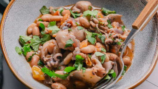 A dish of beans with seafood and cilantro in a bowl, with a fork.