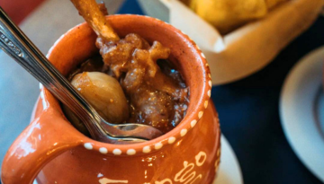Ceramic pot with stew, spoon, and bone, next to a basket of bread.
