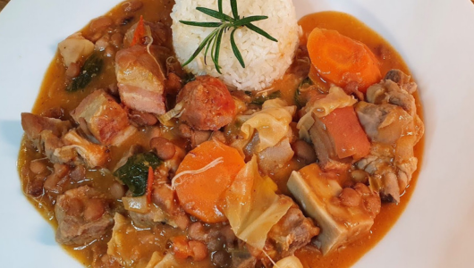 Plate of stew with meat, carrots, beans, cabbage, and rice garnish on top.