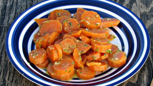 Sliced cooked carrots with herbs served on a striped plate.