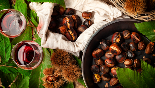 Chestnuts in a pan and fabric bag with two glasses of red wine on green leaves.
