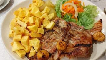 Grilled meat with fried potatoes, lettuce, carrots, and onions on a plate.