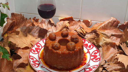 Bundt cake with caramel sauce on a plate, surrounded by autumn leaves, and a glass of red wine.