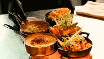 Four dishes in small skillets on a wooden board with crispy toppings and greens.