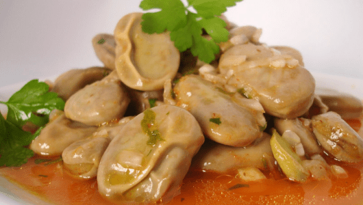 Cooked broad beans in sauce, garnished with parsley leaves on a white plate.