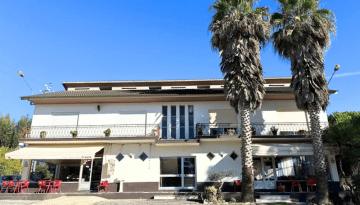 Two-story building with palm trees, outdoor seating, and clear blue sky.
