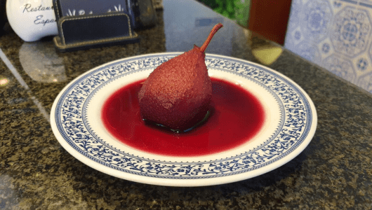 Poached pear in red sauce on a decorative blue and white plate.