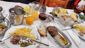 Table with steak, fries, wine, and orange juice on plates.