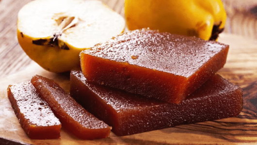 Slices of quince paste on a wooden board next to fresh quince.
