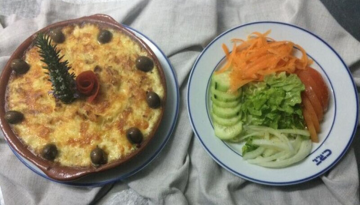 Baked dish with olives next to a salad of carrots, cucumber, and lettuce.