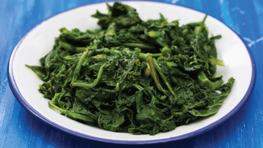 White plate with cooked leafy greens on a blue wooden table.